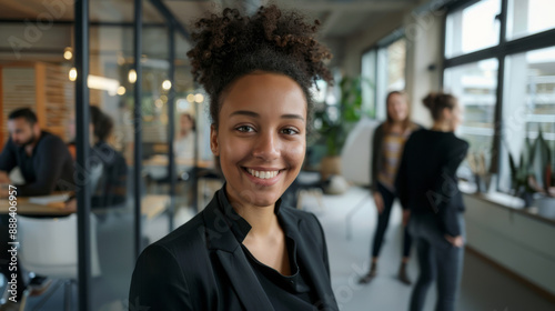 Smiling woman in a bright, modern office, exuding confidence and positivity amidst colleagues.