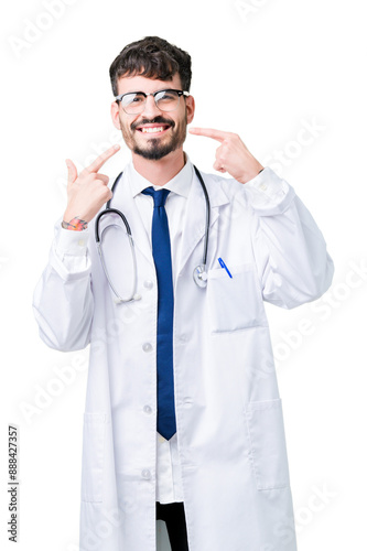 Young doctor man wearing hospital coat over isolated background smiling confident showing and pointing with fingers teeth and mouth. Health concept.