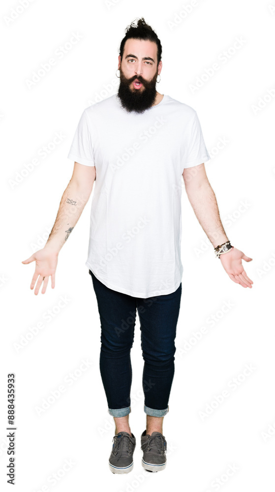 Young hipster man with long hair and beard wearing casual white t-shirt In shock face, looking skeptical and sarcastic, surprised with open mouth Young hipster man with long hair and beard wearing casual white t-shirt In shock face, looking skeptical and sarcastic, surprised with open mouth