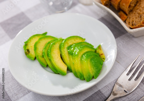 Avocado fruit is peeled and cut into slices on plate. View from above. Healthy, easily digestible snack, fruit food, energy source