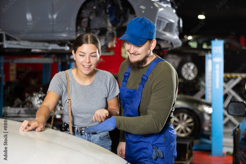 Fototapeta premium Young guy mechanic advises young woman client on repairing of car in car service station