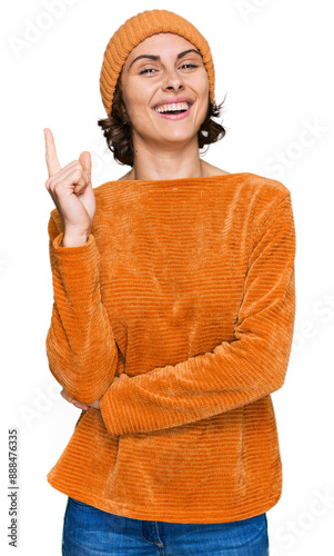 Young hispanic woman wearing casual clothes and wool cap with a big smile on face, pointing with hand and finger to the side looking at the camera.