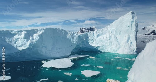 Melting icebergs float turquoise water ocean bay. Towering snowy mountain in background. Giant glacier under blue sky in Antarctica. Global warming, melting ice, climate change. Drone shot close up