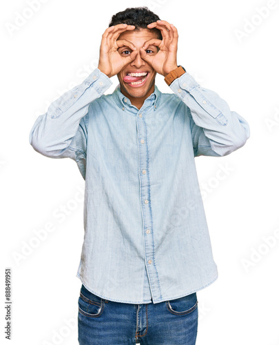 Young handsome african american man wearing casual clothes doing ok gesture like binoculars sticking tongue out, eyes looking through fingers. crazy expression.