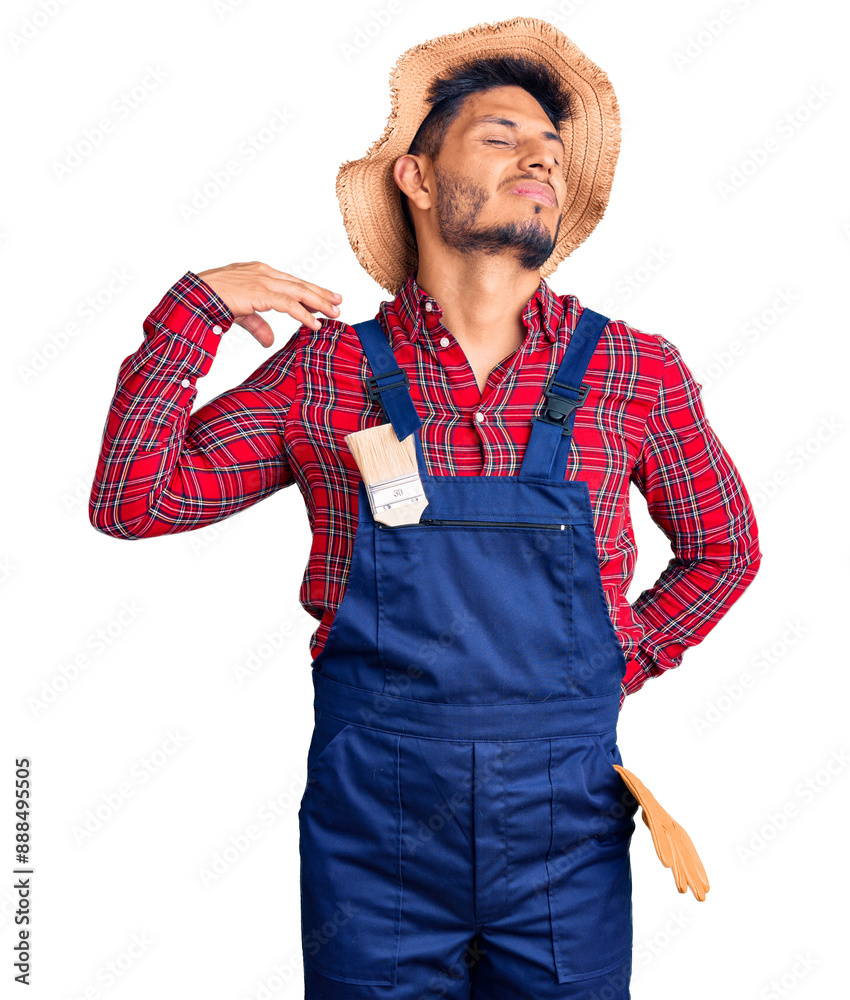 Handsome latin american young man weaing handyman uniform suffering of neck ache injury, touching neck with hand, muscular pain Handsome latin american young man weaing handyman uniform suffering of neck ache injury, touching neck with hand, muscular pain