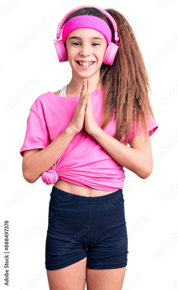 Cute hispanic child girl wearing gym clothes and using headphones praying with hands together asking for forgiveness smiling confident. Cute hispanic child girl wearing gym clothes and using headphones praying with hands together asking for forgiveness smiling confident.