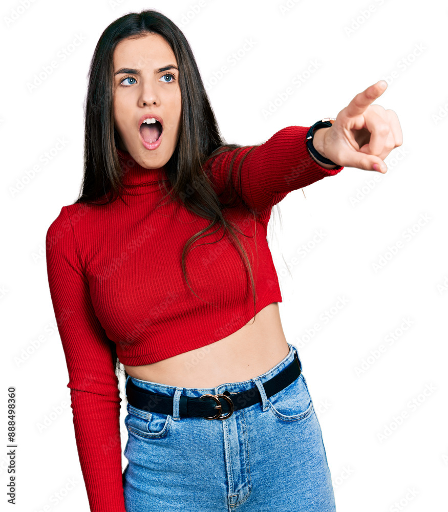 Young brunette teenager wearing red turtleneck sweater pointing with finger surprised ahead, open mouth amazed expression, something on the front Young brunette teenager wearing red turtleneck sweater pointing with finger surprised ahead, open mouth amazed expression, something on the front