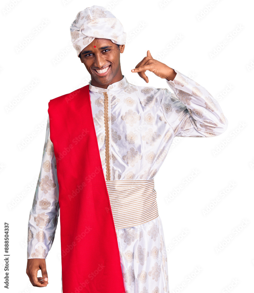 African handsome man wearing tradition sherwani saree clothes smiling doing phone gesture with hand and fingers like talking on the telephone. communicating concepts. African handsome man wearing tradition sherwani saree clothes smiling doing phone gesture with hand and fingers like talking on the telephone. communicating concepts.