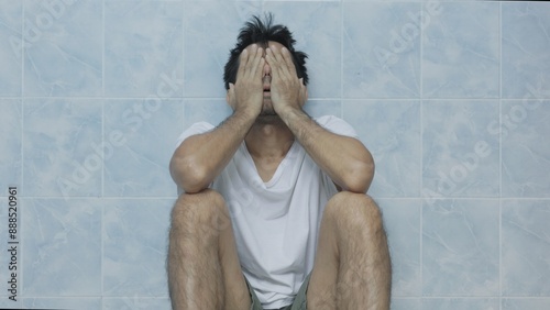 asian man sitting stressed in bathroom alone	