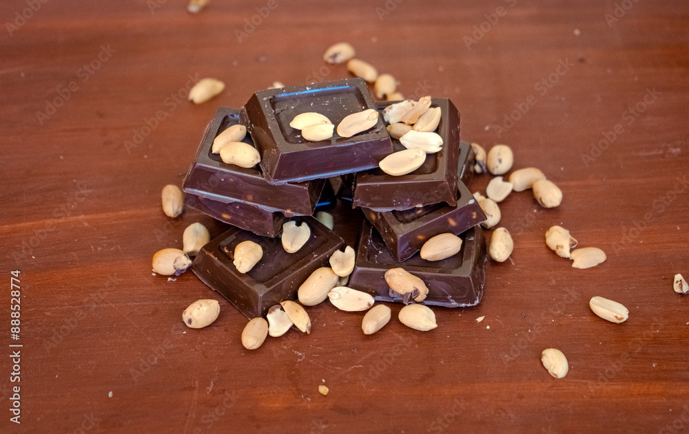 Dark chocolate pieces with peanuts on wooden table background Dark chocolate pieces with peanuts on wooden table background