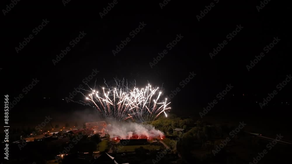 Spectaculaire feu d'artifice illuminant le ciel nocturne avec des éclats dorés et des explosions étincelantes, capturé au-dessus d'une petite ville.