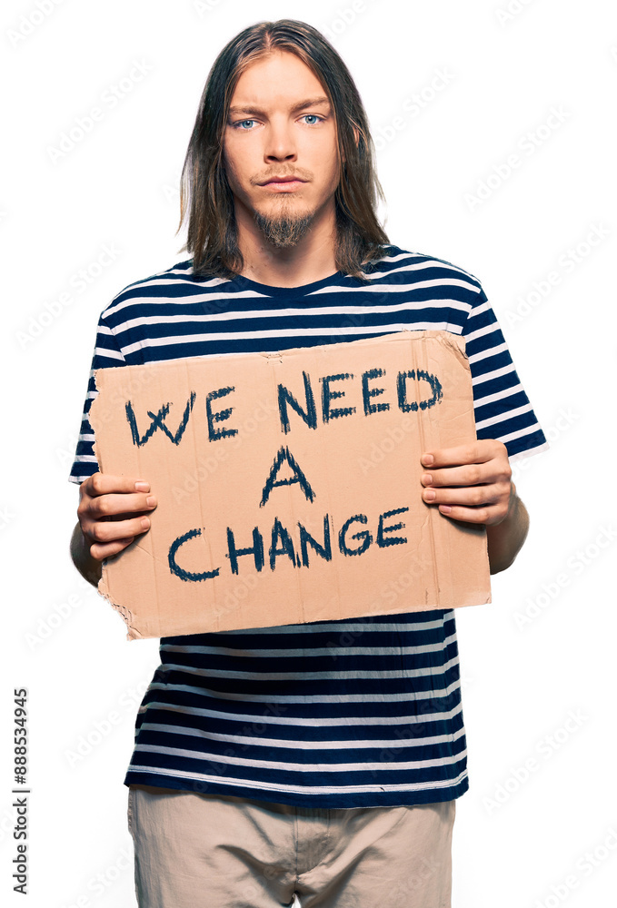 Handsome caucasian man with long hair holding we need a change banner thinking attitude and sober expression looking self confident Handsome caucasian man with long hair holding we need a change banner thinking attitude and sober expression looking self confident