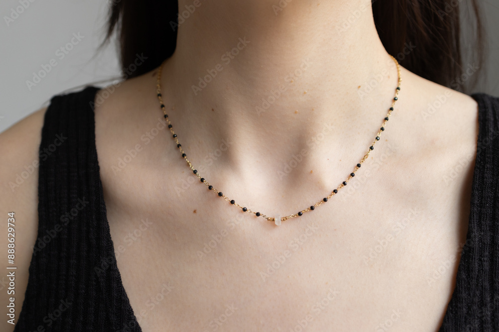 Simple beaded necklace on female neck. Model posing with jewelry in black top. Elegant pendant on young woman chest Simple beaded necklace on female neck. Model posing with jewelry in black top. Elegant pendant on young woman chest