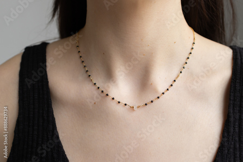 Simple beaded necklace on female neck. Model posing with jewelry in black top. Elegant pendant on young woman chest