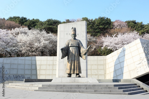 Paldal-gu, Suwon-si, Gyeonggi-do, South Korea - April 2, 2023: Front view of bronze statue of King Jeongjo against stone monument and white cherry blossoms at Paldalsan Mountain
 photo