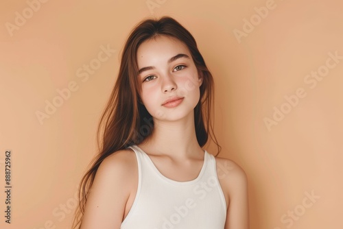 Portrait of a charming pretty teenage girl with a lovely hairstyle looking glad and attractive in a white top singing on a pastel beige background © LimeSky