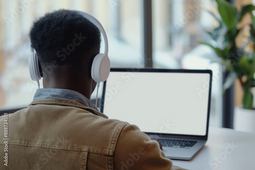 A young african american man sitting in front of a white laptop screen in his room back to camera photo