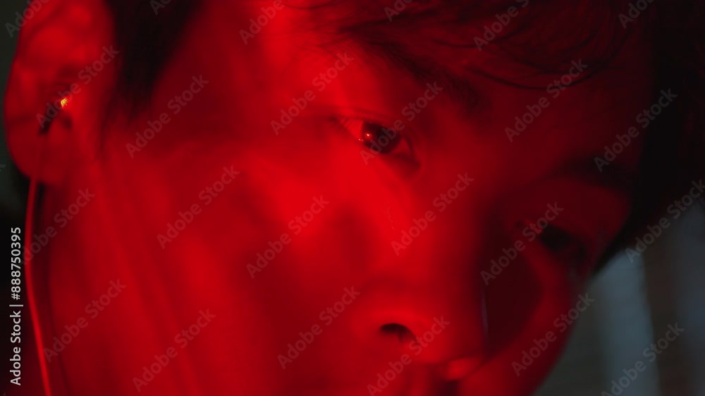 close up of asiatic young male with soft red neon light listening to music with earphone close up of asiatic young male with soft red neon light listening to music with earphone