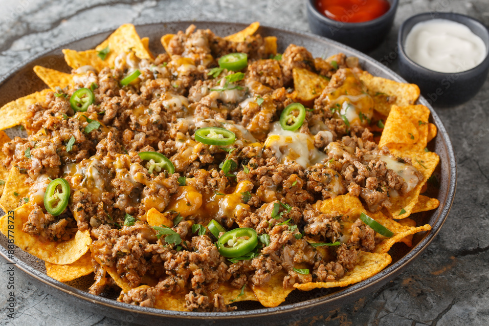 Corn nachos with lots of stewed minced meat, cheddar cheese and jalapeno pepper served with sauces closeup on the plate on the table. Horizontal Corn nachos with lots of stewed minced meat, cheddar cheese and jalapeno pepper served with sauces closeup on the plate on the table. Horizontal