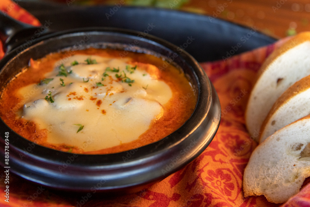 a warm bowl of creamy Colombian tomato soup au gratin garnished with a swirl of cream and fresh basil leaves served in a rustic earthenware dish with garlic bread on a tray a warm bowl of creamy Colombian tomato soup au gratin garnished with a swirl of cream and fresh basil leaves served in a rustic earthenware dish with garlic bread on a tray