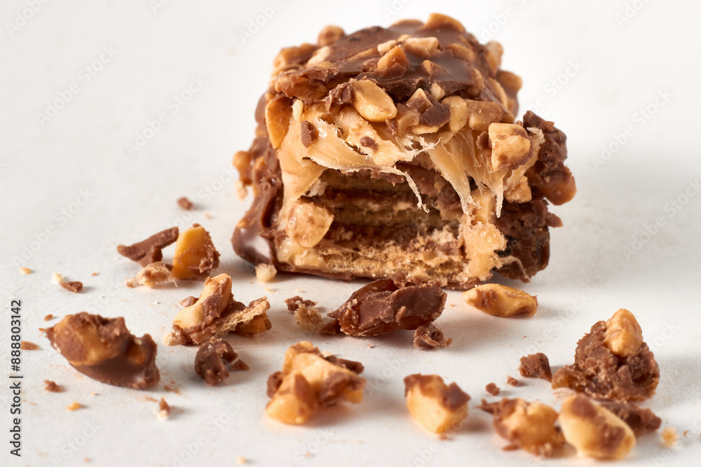Broken piece of chocolate wafer bar with nuts and caramel in cut and crumbs isolated on white background Broken piece of chocolate wafer bar with nuts and caramel in cut and crumbs isolated on white background