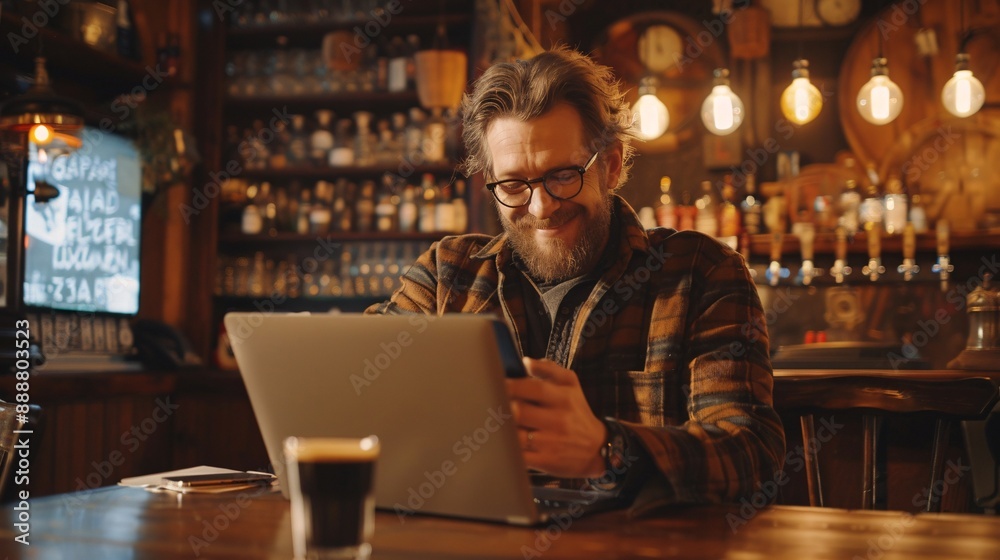 Content man utilizing cellphone while working on computer in a bar. Content man utilizing cellphone while working on computer in a bar.
