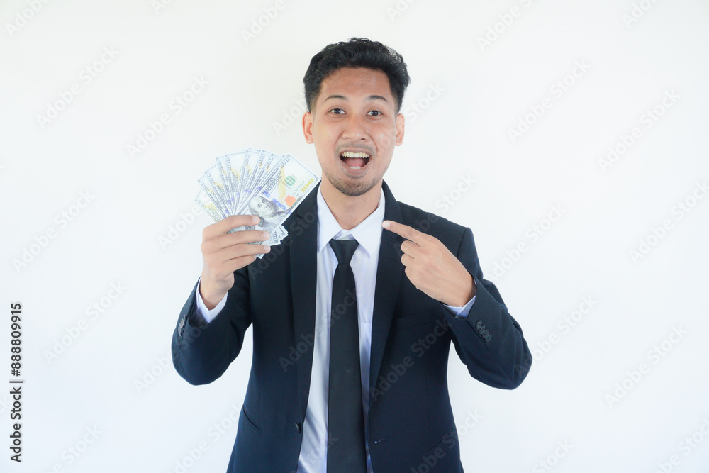 Portrait of an excited young man dressed in suit pointing finger at bunch of money banknotes isolated over white background Portrait of an excited young man dressed in suit pointing finger at bunch of money banknotes isolated over white background