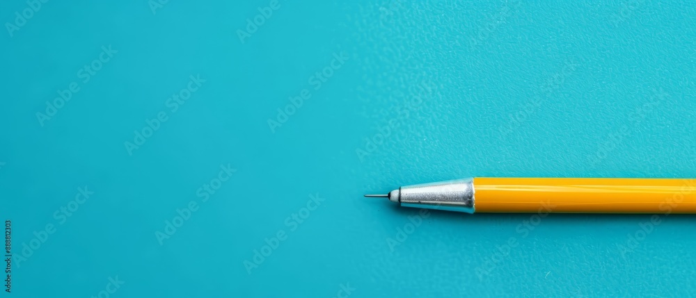 A yellow ballpoint pen rests atop a bright blue surface, with its tip prominent in the foreground A yellow ballpoint pen rests atop a bright blue surface, with its tip prominent in the foreground