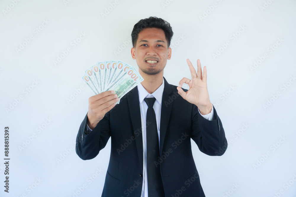 Smiling man shows money cash and excellent sign, demonstrating that everything is fine. Photo of asian man wearing black suit on white background. Emotions and pleasant feelings concept. Smiling man shows money cash and excellent sign, demonstrating that everything is fine. Photo of asian man wearing black suit on white background. Emotions and pleasant feelings concept.