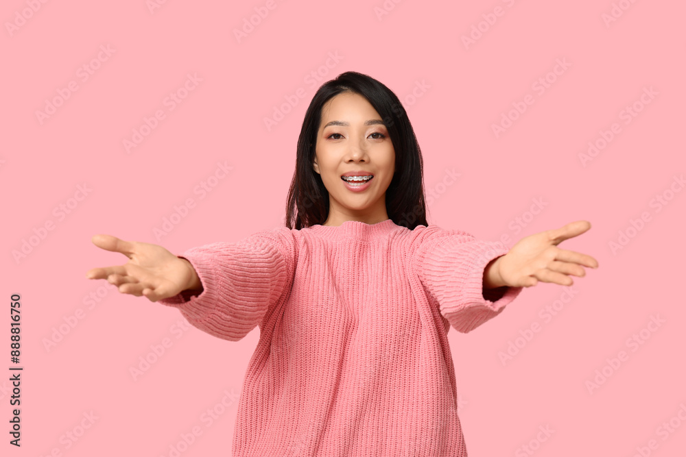 Young Asian woman opening arms for hug on pink background