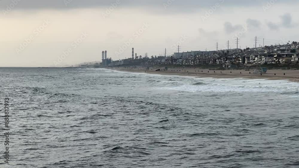 Rolling waves towards the multi-million dollar mansion lined Manhattan Beach coastline with a steam power plant visible in the distant on a cloud and gloomy day Rolling waves towards the multi-million dollar mansion lined Manhattan Beach coastline with a steam power plant visible in the distant on a cloud and gloomy day