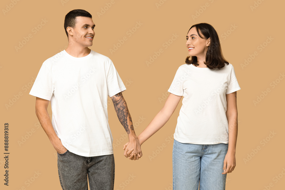 Young couple holding hands and smiling at each other on beige background Young couple holding hands and smiling at each other on beige background