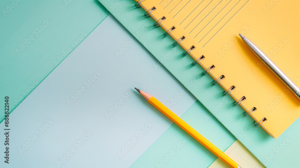 A yellow notepad, silver pen, and yellow pencil sit on a pastel green and light blue background A yellow notepad, silver pen, and yellow pencil sit on a pastel green and light blue background
