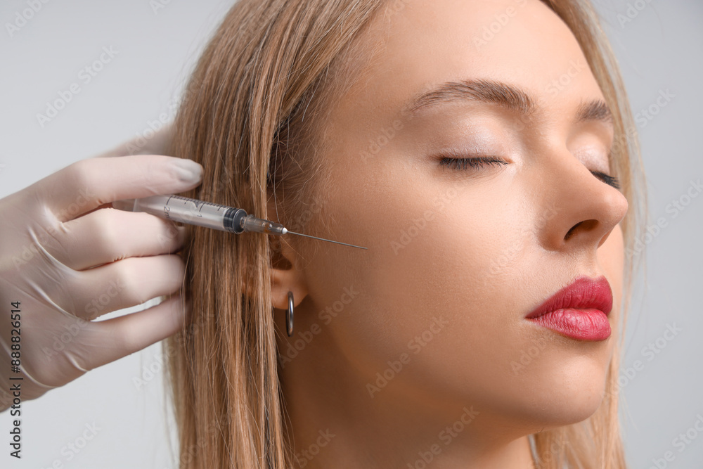 Young woman receiving filler injection in face against grey background. Skin care concept Young woman receiving filler injection in face against grey background. Skin care concept