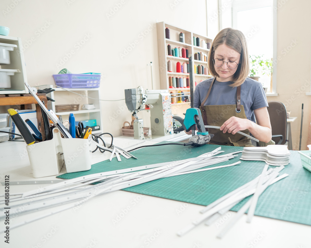 Obraz premium Woman tanner processes the edges of a leather belt in a workshop. 