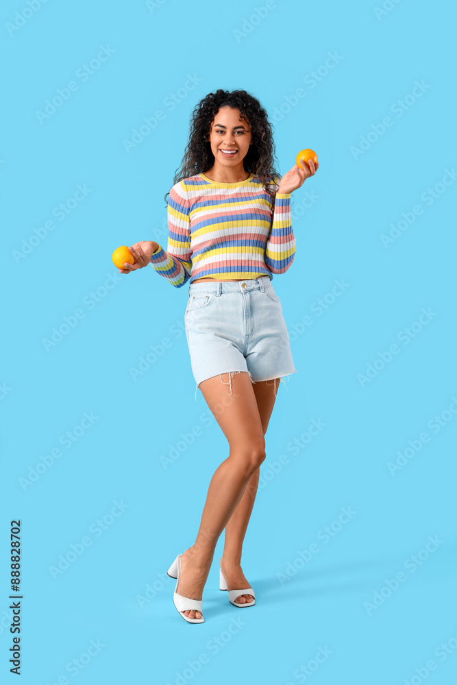 Young African-American woman with oranges on blue background Young African-American woman with oranges on blue background