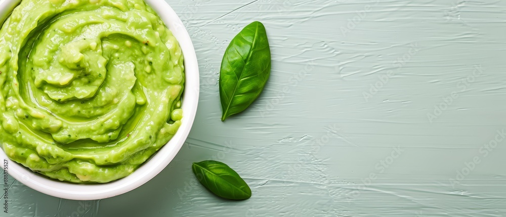 Obraz premium A white bowl holds green guacamole, accompanied by a green basil sprig
