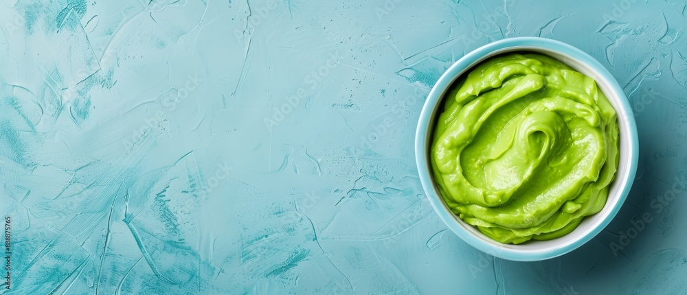 Obraz premium A blue backdrop features a tablecloth in shades of white and blue Atop it sits a filled bowl of vibrant green guacamole