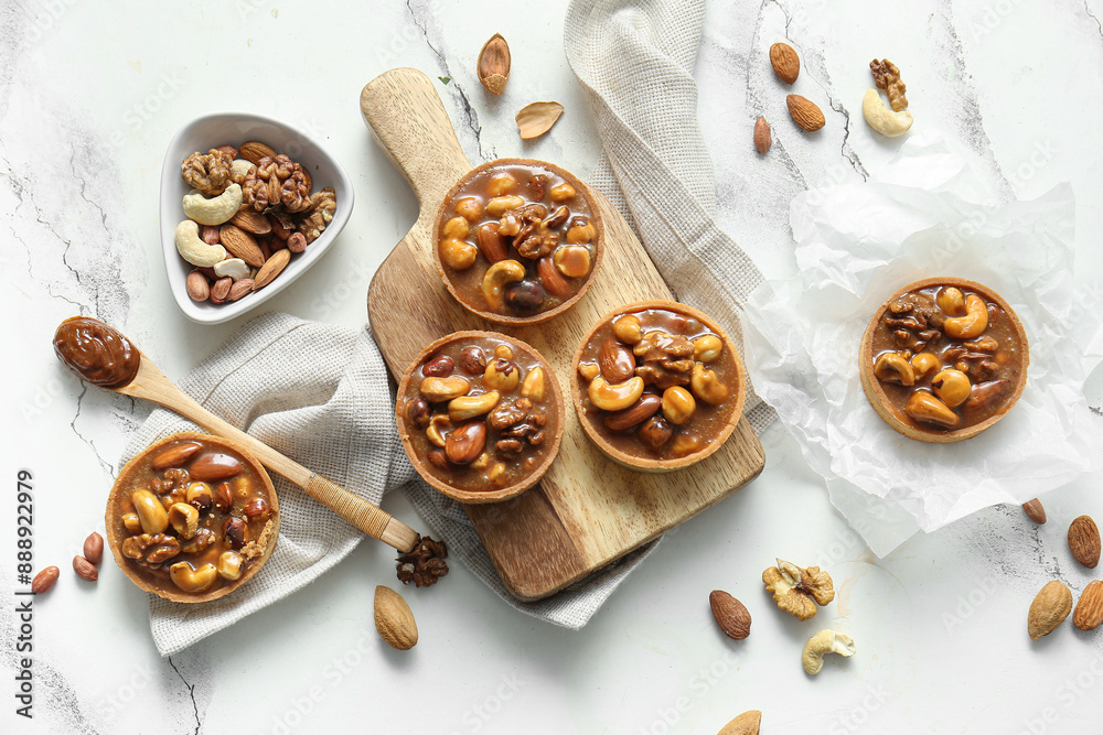 Tasty tarts with different nuts and caramel on wooden board against grunge white background Tasty tarts with different nuts and caramel on wooden board against grunge white background