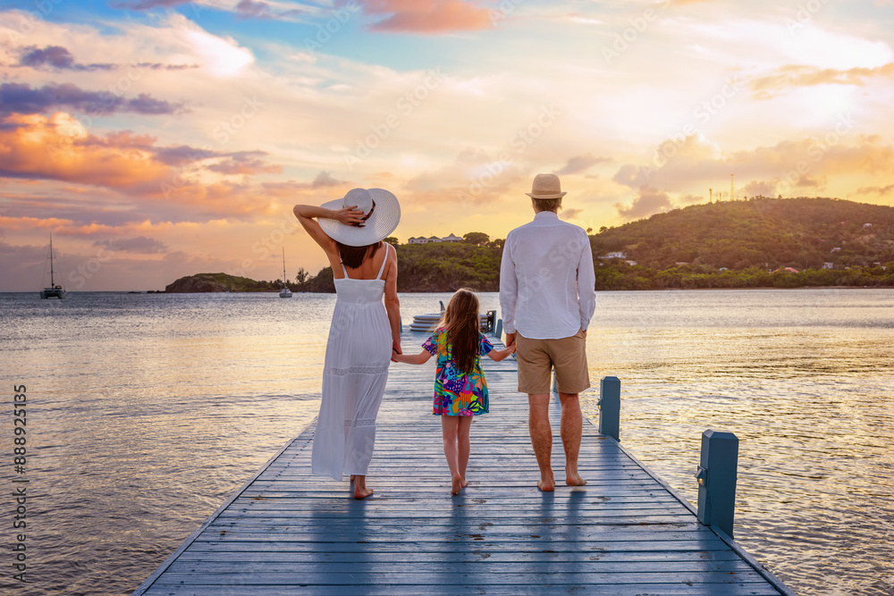 A family walks down a pier in the Caribbean sea during beautiful sunset time at their holiday vacations