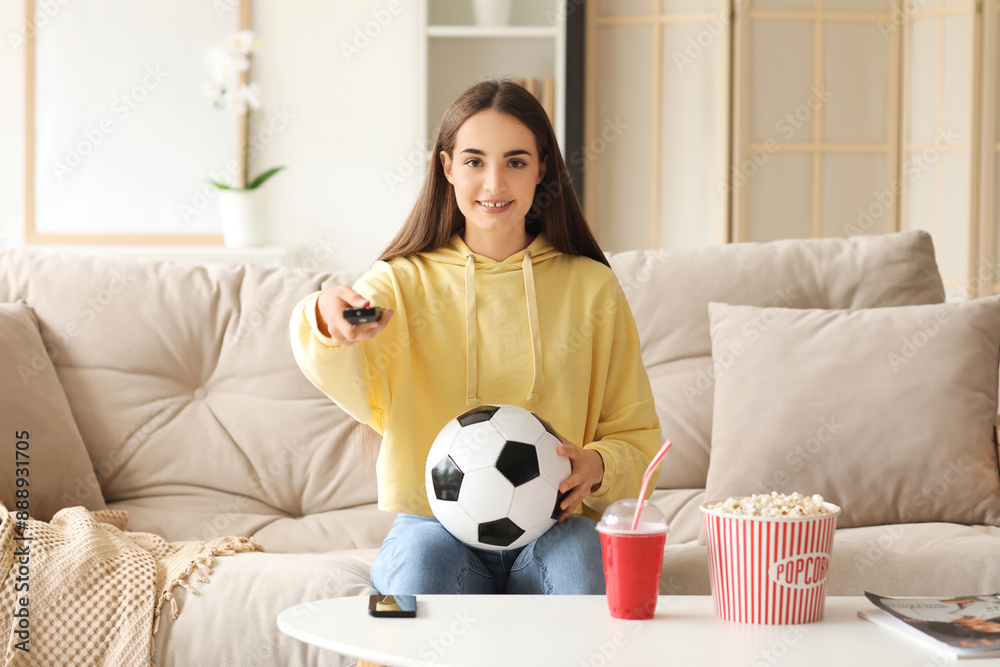 Beautiful young happy woman with soccer ball, cup of cola and popcorn watching football on TV at home Beautiful young happy woman with soccer ball, cup of cola and popcorn watching football on TV at home