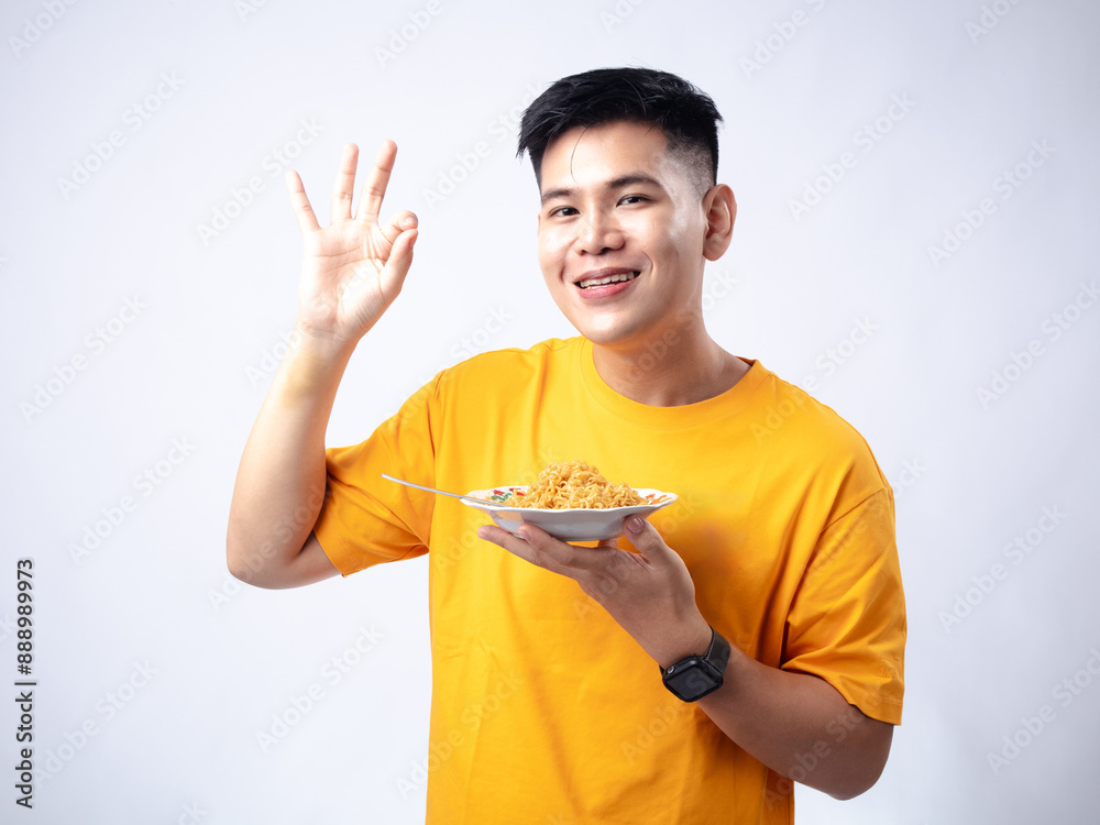 Chinese Indonesian man in yellow shirt picking up fried noodles with fork from a white plate, while smiling and closing his eyes. Isolated in white background. Chinese Indonesian man in yellow shirt picking up fried noodles with fork from a white plate, while smiling and closing his eyes. Isolated in white background.