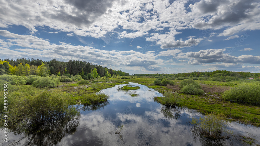A picturesque springtime view of a winding river flowing through a lush forest, with the blue sky and puffy white clouds reflected in the still water. A picturesque springtime view of a winding river flowing through a lush forest, with the blue sky and puffy white clouds reflected in the still water.