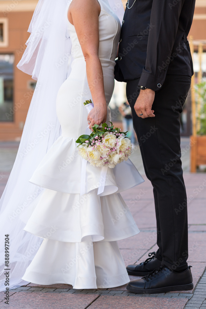 The bride stands opposite the groom. Photo of the bride and groom without faces. The bride holds a bouquet in her hand. Stylish wedding photo. The bride's long veil trails along the ground. Beautiful The bride stands opposite the groom. Photo of the bride and groom without faces. The bride holds a bouquet in her hand. Stylish wedding photo. The bride's long veil trails along the ground. Beautiful