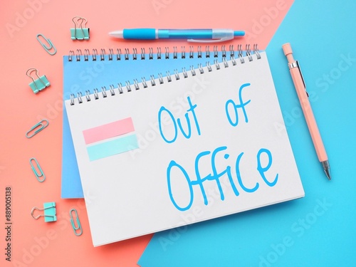 Vibrant composition with a blue paper with the handwritten words out of office on a pink background next to a pair of pens. Colorful out-of-office message in pastel colors