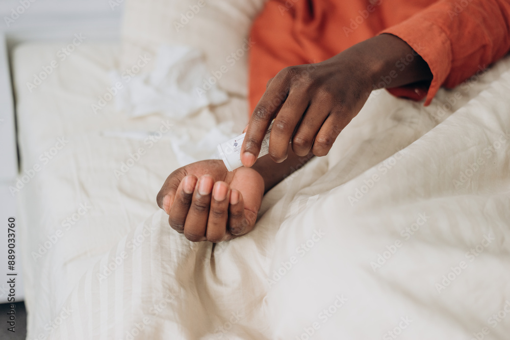 Close-up of man hand taking medication in bed, highlighting self-care and health management in a cozy, indoor setting. Close-up of man hand taking medication in bed, highlighting self-care and health management in a cozy, indoor setting.