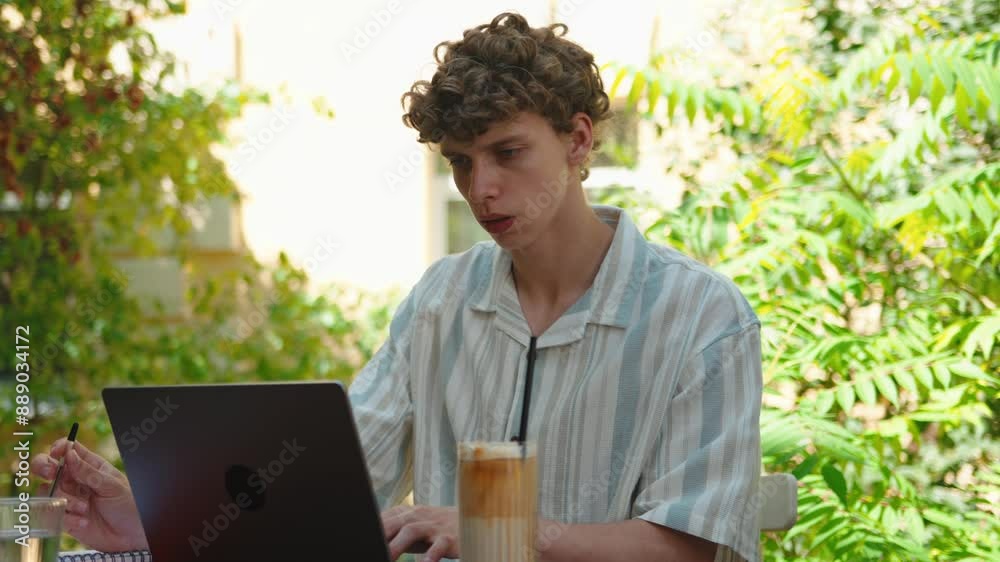 Handsome curly man teenager student using pc computer laptop, working on project, studying outdoors at cafe on terrace. Comfort workplace. Distance education concept, freelancer, work Handsome curly man teenager student using pc computer laptop, working on project, studying outdoors at cafe on terrace. Comfort workplace. Distance education concept, freelancer, work