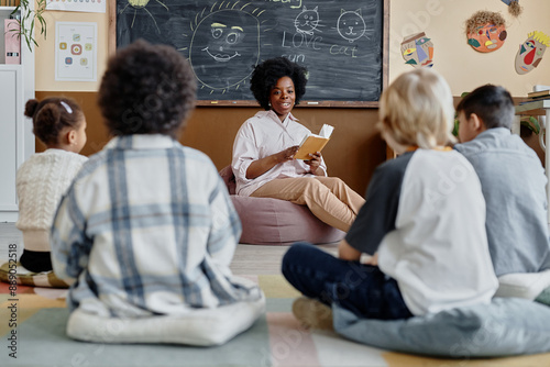 Obraz na plátne Young female teacher of Black ethnicity in bean bag chair reading book together