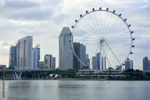 Modern city skyline with towering skyscrapers and a large observation wheel by the waterfront under a cloudy sky. photo