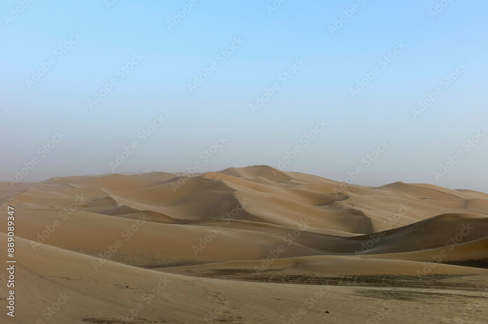 Smooth sand dunes under a hazy sky in a vast desert landscape. Smooth sand dunes under a hazy sky in a vast desert landscape.
